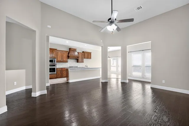 a view of an empty room with wooden floor and a kitchen