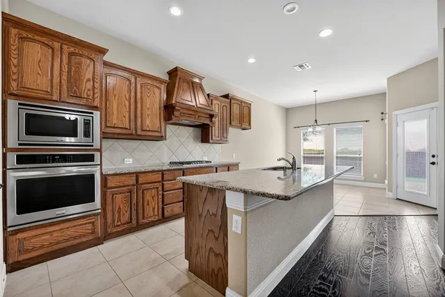 a kitchen with stainless steel appliances granite countertop a stove top oven a sink dishwasher a dining table and chairs with wooden floor