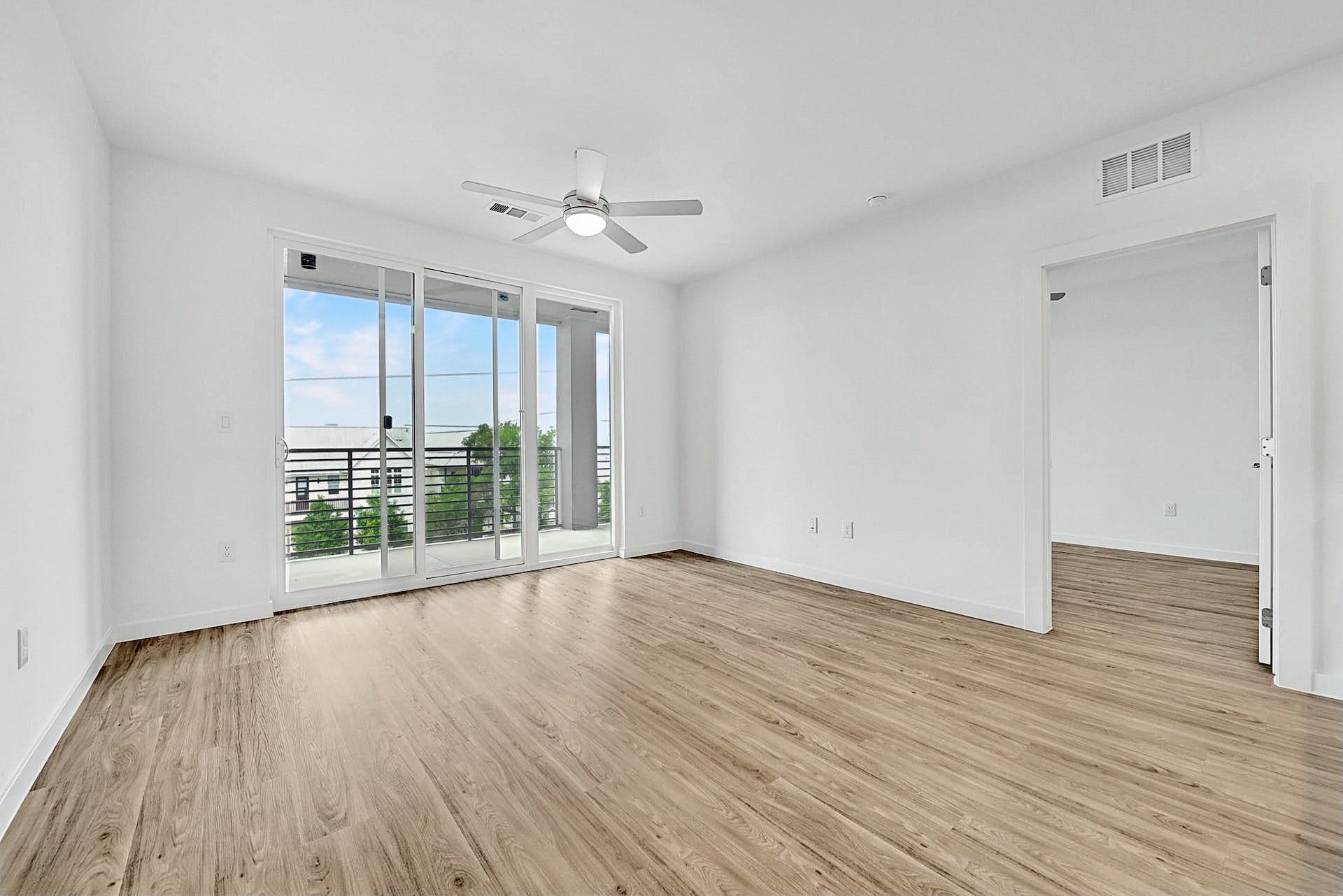 4801 Springdale Road, Unit 1301 Austin, TX 78723 - Photo 12 of 39 A spacious room with warm wood flooring and a wide sliding glass door opening to an outdoor balcony.