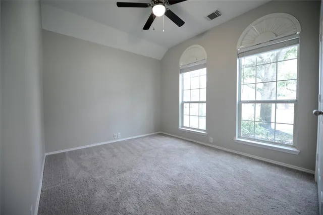 an empty room with chandelier fan and windows