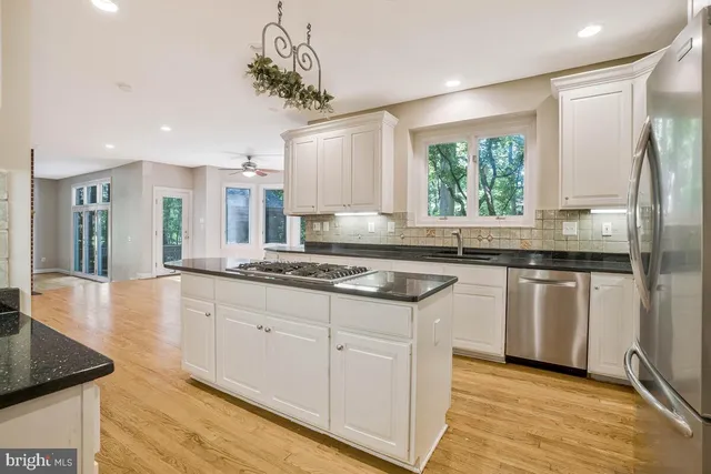 a kitchen with stainless steel appliances granite countertop a sink dishwasher a refrigerator and white cabinets with wooden floor