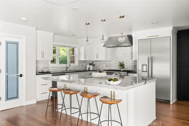 a kitchen with stainless steel appliances kitchen island granite countertop a refrigerator a stove a sink and chairs with wooden floor