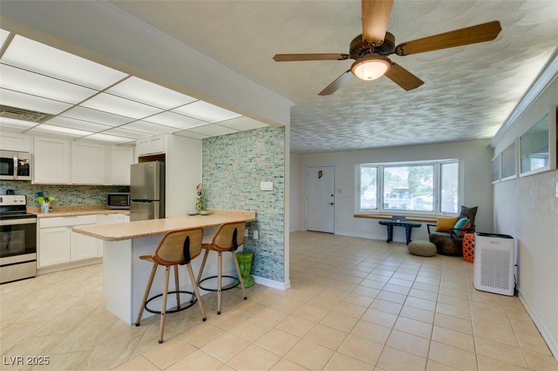 4087 Pleasant Road Las Vegas, NV 89108 - Photo 22 of 74 Kitchen featuring appliances with stainless steel finishes, decorative backsplash, light tile patterned flooring, white cabinets, and crown molding
