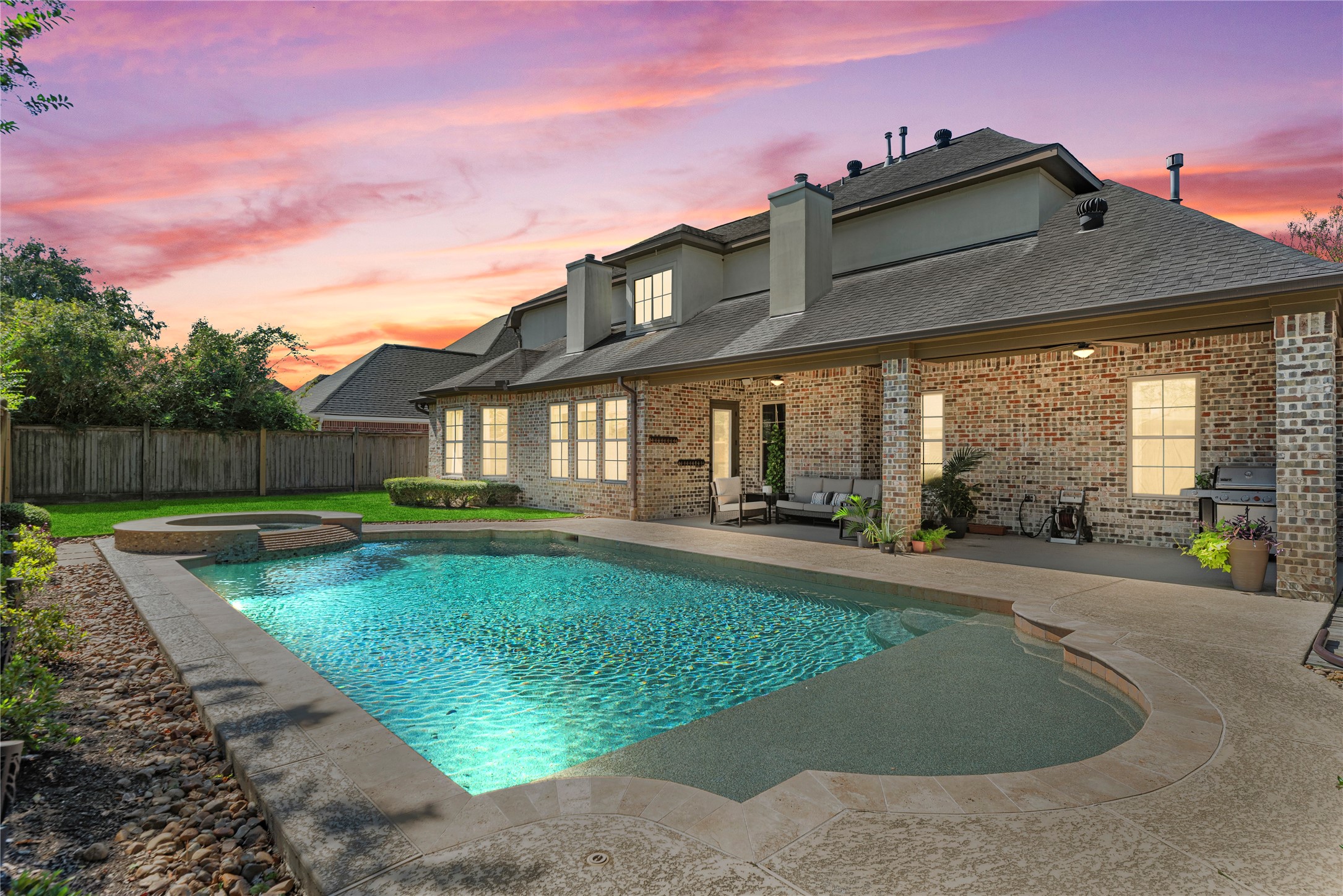 Resort-style backyard retreat! Enjoy your own private oasis featuring a sparkling pool with raised spa and waterfall spillway, all set against a stunning sunset backdrop. The spacious covered patio extends your living area outdoors — perfect for relaxing or entertaining in style.