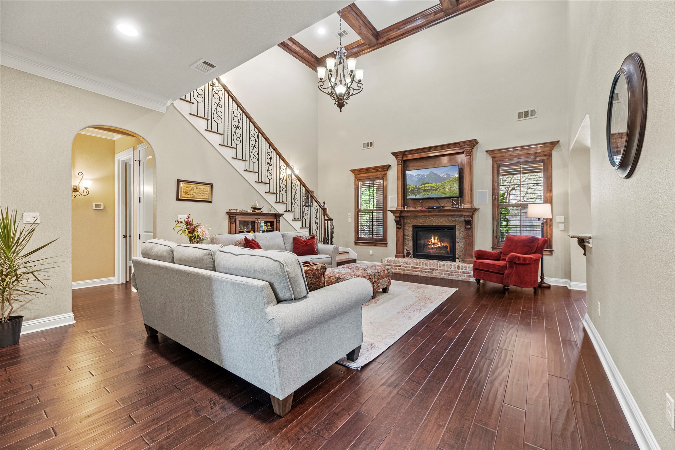 3550 Windrose Drive Beaumont, TX 77706 - Photo 16 of 50 Impressive two-story living room with hand-scraped luxury engineered wood floors, elegant wrought-iron staircase, and a rich wood-trimmed gas fireplace. Coffered ceiling with chandelier adds dramatic architectural character.