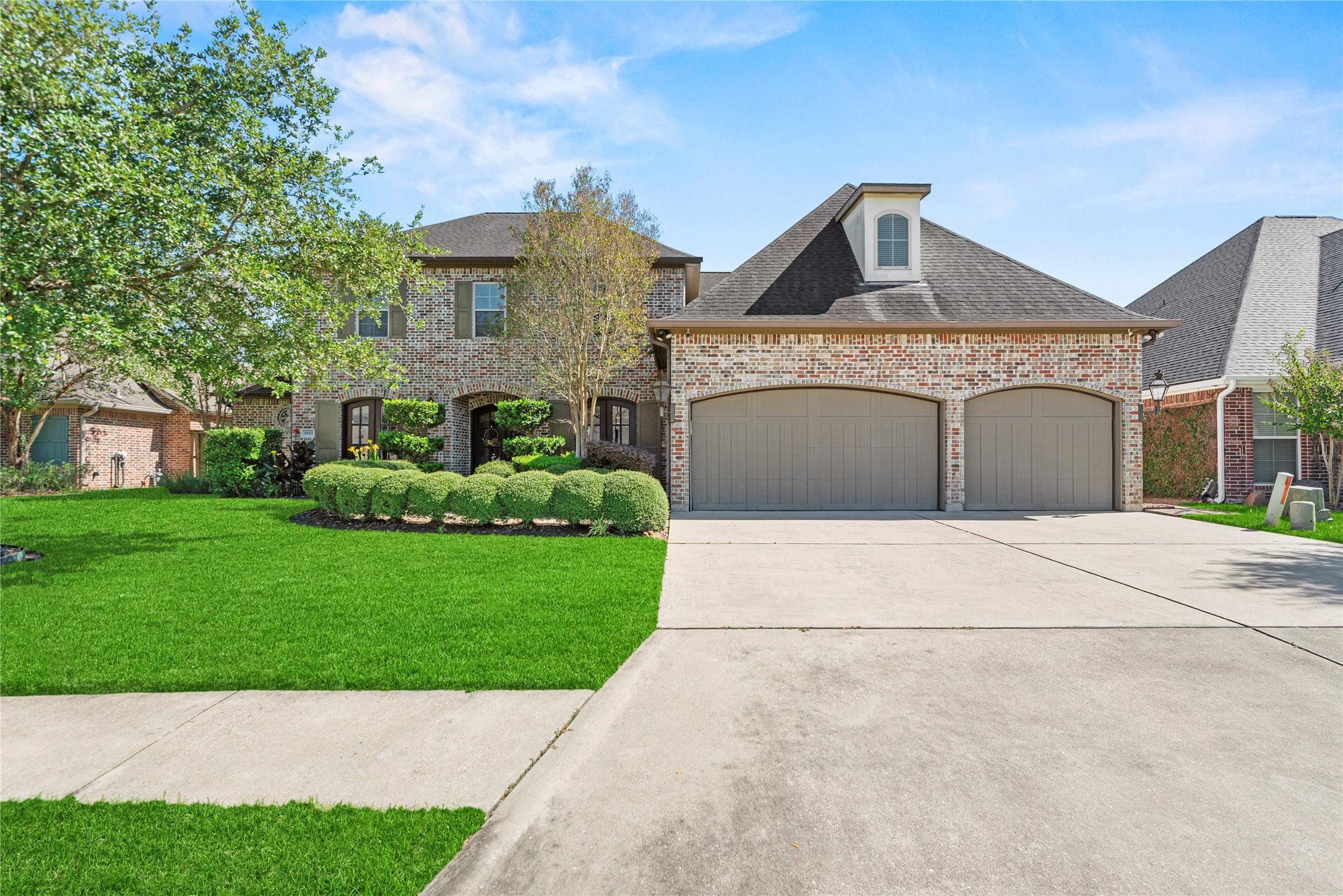 3550 Windrose Drive Beaumont, TX 77706 - Photo 8 of 50 Beautiful daytime view of the home’s classic brick exterior and triple-garage design, framed by lush green lawn and mature trees. The wide driveway offers ample parking and a welcoming approach.