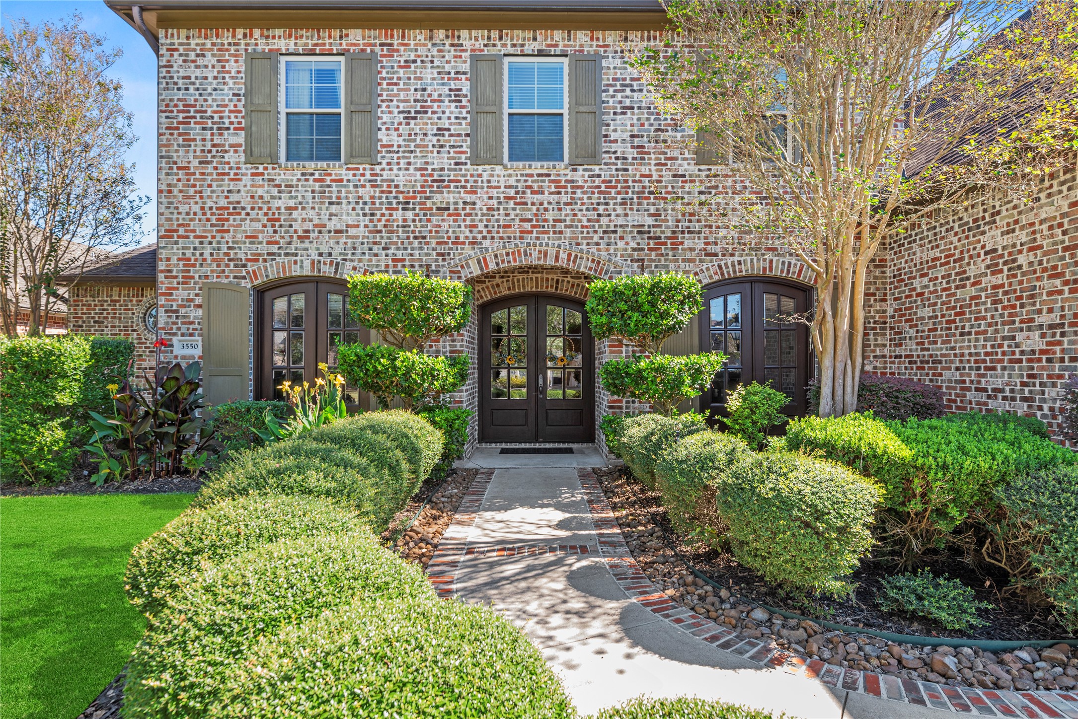 3550 Windrose Drive Beaumont, TX 77706 - Photo 10 of 50 Inviting front path lined with perfectly trimmed hedges and flowering plants leads to the arched double doors — a warm and elegant first impression for guests. Two classic gas lanterns softly illuminate the entryway, enhancing the home’s timeless curb appeal.