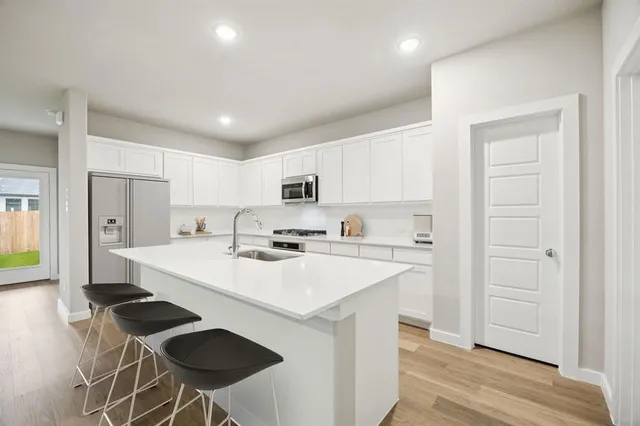 a kitchen with a sink a stove a refrigerator and white cabinets with wooden floor