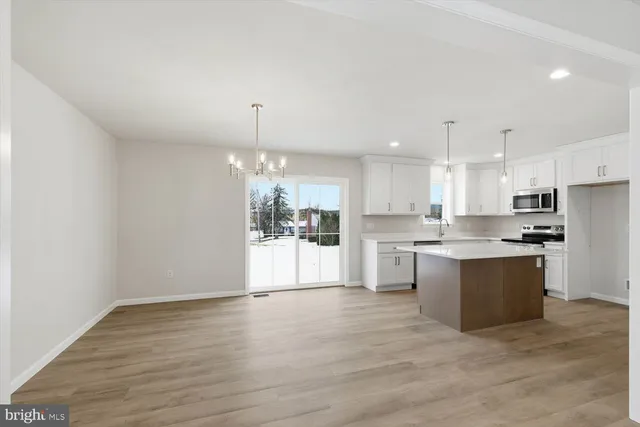 a large white kitchen with kitchen island a sink dishwasher a refrigerator and white cabinets with wooden floor