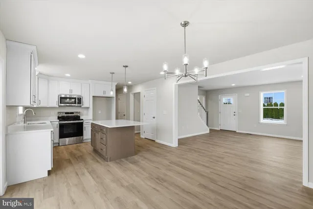 a view of an empty room and kitchen with wooden floor