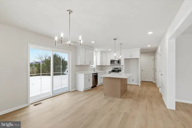 a large white kitchen with a refrigerator a sink dishwasher a stove and a dining table with wooden floor