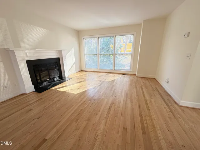 an empty room with wooden floor fireplace and windows