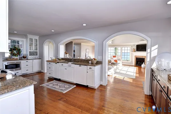 a kitchen with stainless steel appliances granite countertop a stove top oven a sink a refrigerator white cabinets and wooden floor