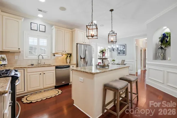a kitchen with stainless steel appliances granite countertop a refrigerator a sink dishwasher a stove a dining table and chairs with wooden floor