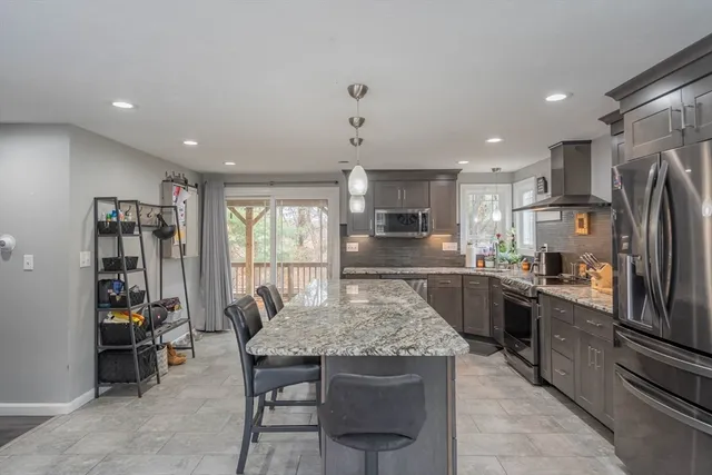 a kitchen with stainless steel appliances kitchen island granite countertop a table chairs refrigerator and microwave