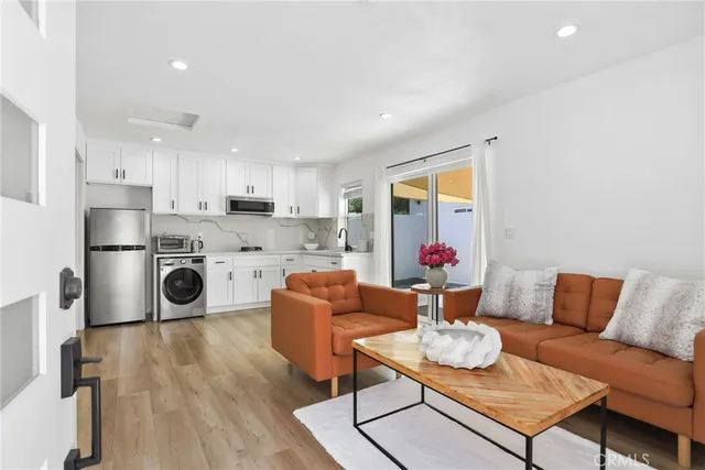 a living room with stainless steel appliances furniture a rug and a kitchen view