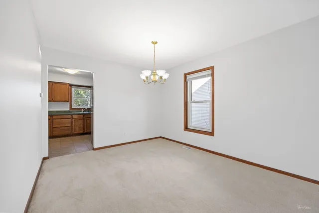 an empty room with chandelier fan and kitchen view