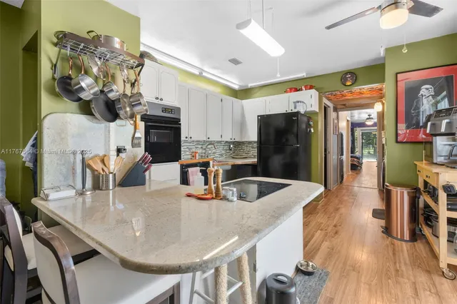 a kitchen with stainless steel appliances granite countertop a kitchen island a stove a refrigerator a dining table and chairs with wooden floor