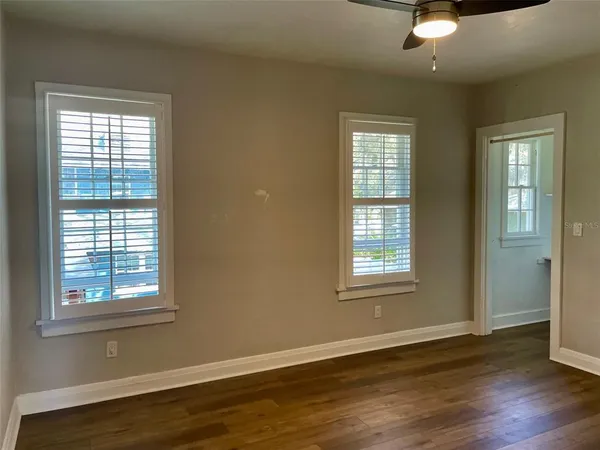 an empty room with wooden floor chandelier fan and windows