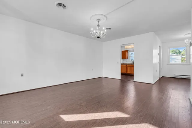 an empty room with wooden floor chandelier and windows