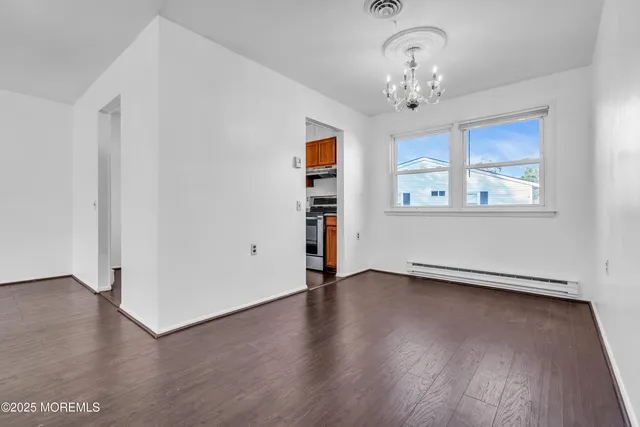 an empty room with wooden floor chandelier and windows