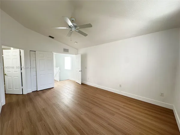 a view of an empty room with wooden floor and a ceiling fan
