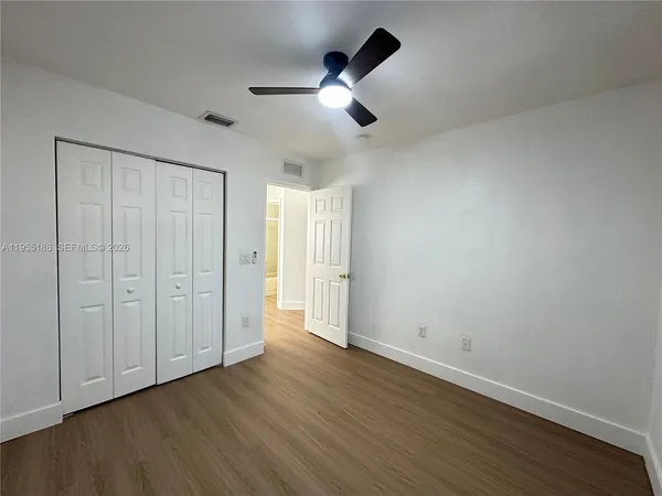 an empty room with wooden floor ceiling fan and windows