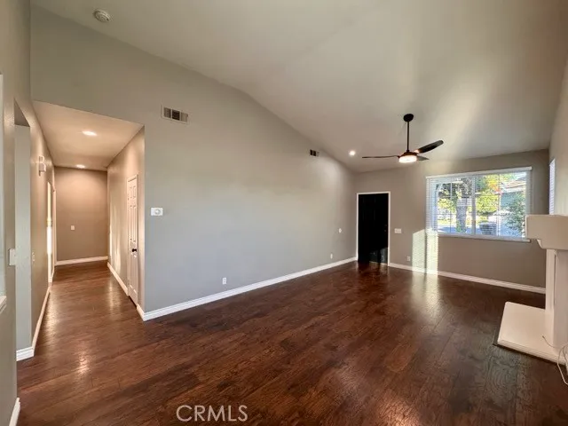 a view of an empty room with wooden floor and a kitchen