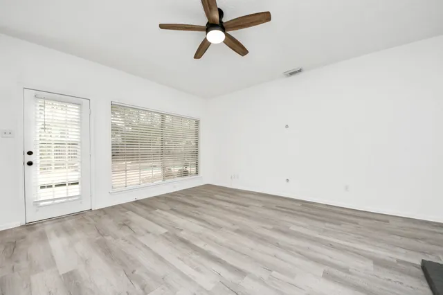 an empty room with chandelier fan and windows