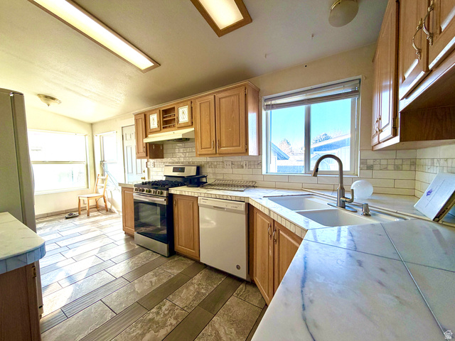 1025 North 300 West, Unit 1 Springville, UT 84663 - Photo 10 of 35 Kitchen with appliances with stainless steel finishes, healthy amount of natural light, under cabinet range hood, vaulted ceiling, and tile countertops