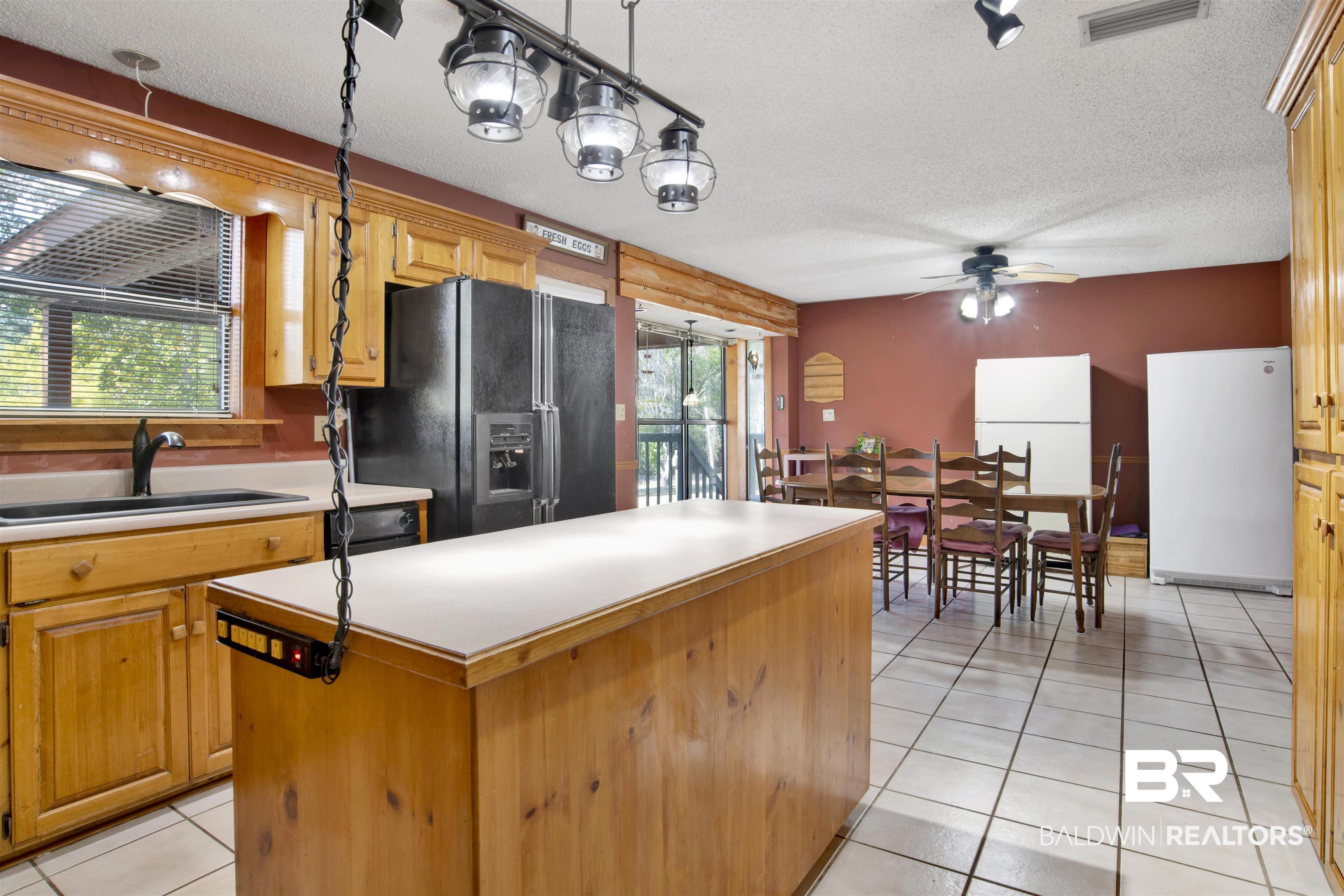 4890 Red Creek Road Semmes, AL 36575 - Photo 14 of 47 Kitchen with light tile patterned floors, a kitchen island, black fridge with ice dispenser, sink, and white refrigerator