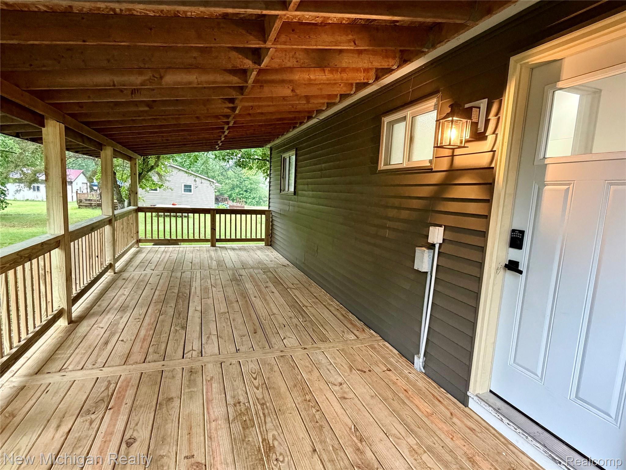 7104 Willard Road Millington, MI 48746 - Photo 8 of 30 Expansive covered porch featuring wood decking and railings, dark siding, an exterior light fixture, and a white entry door