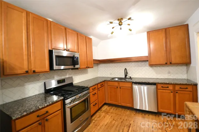 a kitchen with stainless steel appliances granite countertop wooden cabinets a stove a sink and dishwasher with wooden floor