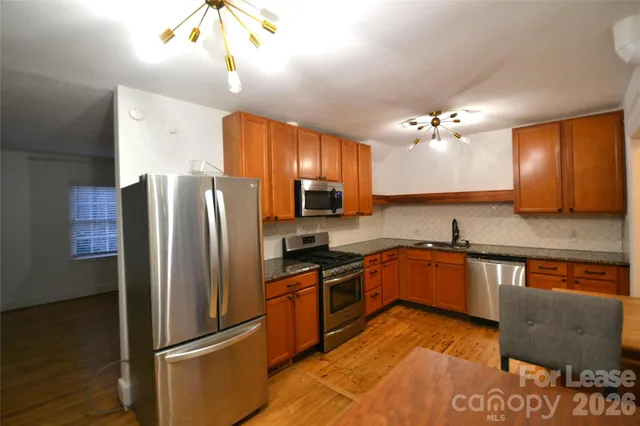 a kitchen with stainless steel appliances granite countertop a refrigerator a sink dishwasher a stove a dining table and chairs with wooden floor