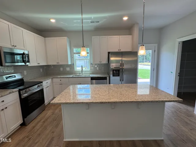 a kitchen with kitchen island granite countertop stainless steel appliances a stove refrigerator a sink and microwave