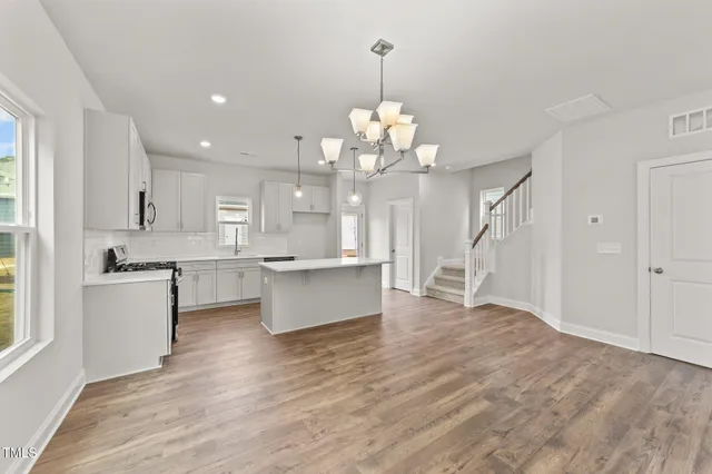 a large kitchen with kitchen island a island a stove a sink dishwasher and white cabinets with wooden floor