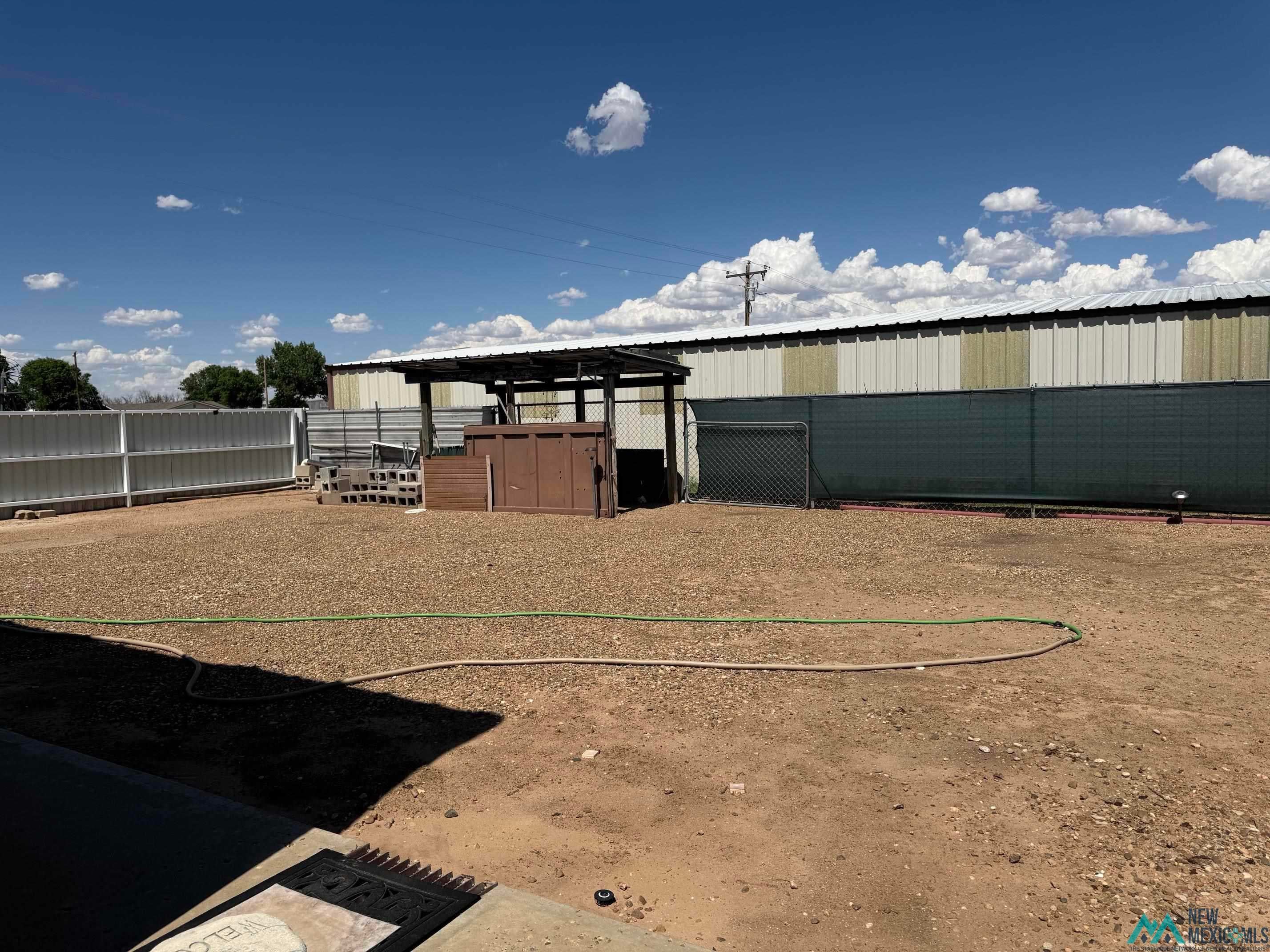 4010 540th Loop Logan, NM 88426 - Photo 27 of 38 Expansive gravel yard featuring a metal shed structure, chain link fencing, and a covered patio area