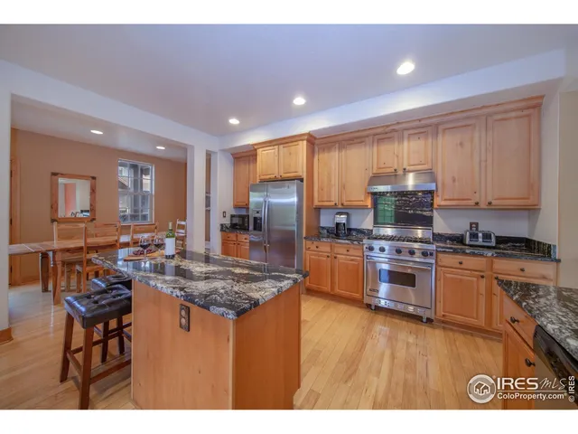 a kitchen with stainless steel appliances granite countertop a stove top oven a sink dishwasher a dining table and chairs with wooden floor