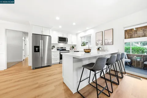 a kitchen with stainless steel appliances a refrigerator a stove a sink a dining table and chairs with wooden floor