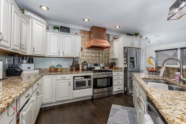 a kitchen with stainless steel appliances granite countertop a stove top oven a sink dishwasher and a refrigerator with wooden cabinets