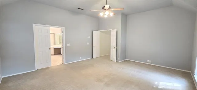 an empty room with chandelier fan and kitchen view