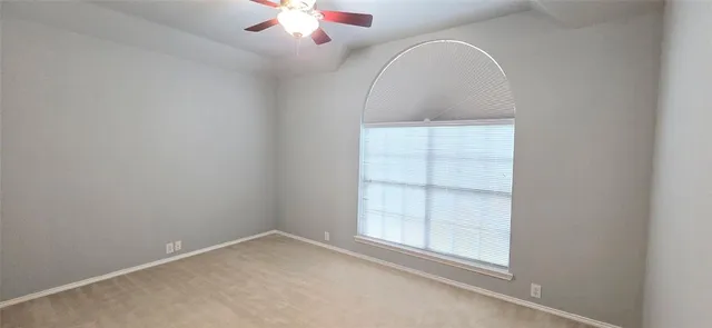 an empty room with a chandelier fan and windows