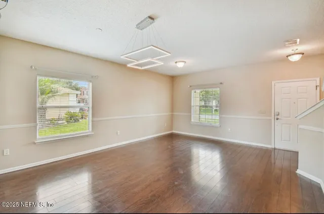 an empty room with wooden floor chandelier fan and windows