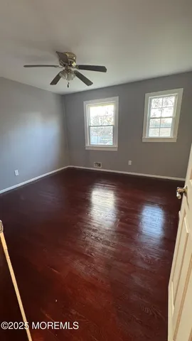 an empty room with wooden floor chandelier fan and windows