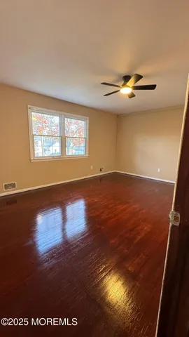 an empty room with wooden floor chandelier fan and windows