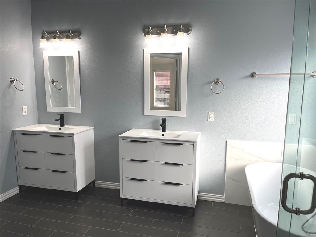 4101 White Porch Road Plano, TX 75024 - Photo 12 of 18 Master bathroom featuring dual modern vanities with integrated sinks and matte black faucets, overhead vanity lighting, dark tile flooring, and a freestanding soaking tub with a glass enclosure