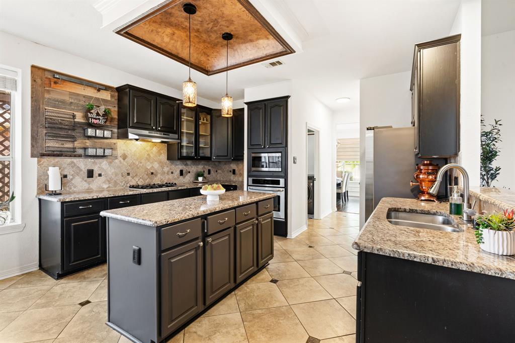 3905 Lakeside Drive Rowlett, TX 75088 - Photo 22 of 39 Kitchen featuring a kitchen island, light stone countertops, dark cabinetry, pendant lighting, and light tile patterned floors