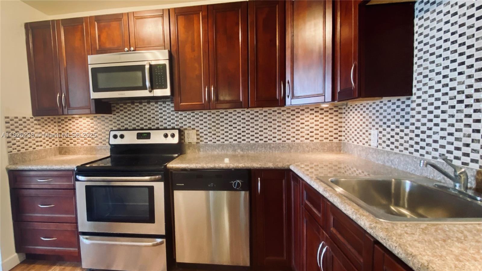 2025 Northeast 164th Street, Unit 901 North Miami Beach, FL 33162 - Photo 2 of 12 a kitchen with granite countertop wood cabinets and stainless steel appliances