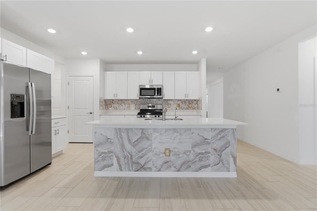 2455 Lanier Road Zephyrhills, FL 33541 - Photo 13 of 39 a large kitchen with stainless steel appliances kitchen island granite countertop a refrigerator a stove a sink a microwave and white cabinets with wooden floor