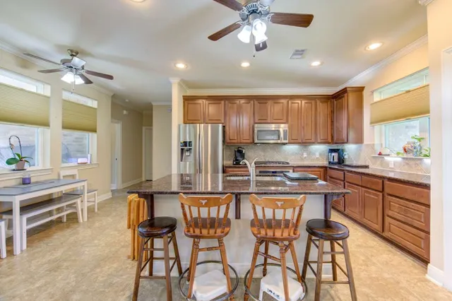 a kitchen with stainless steel appliances kitchen island granite countertop a dining table chairs and a refrigerator